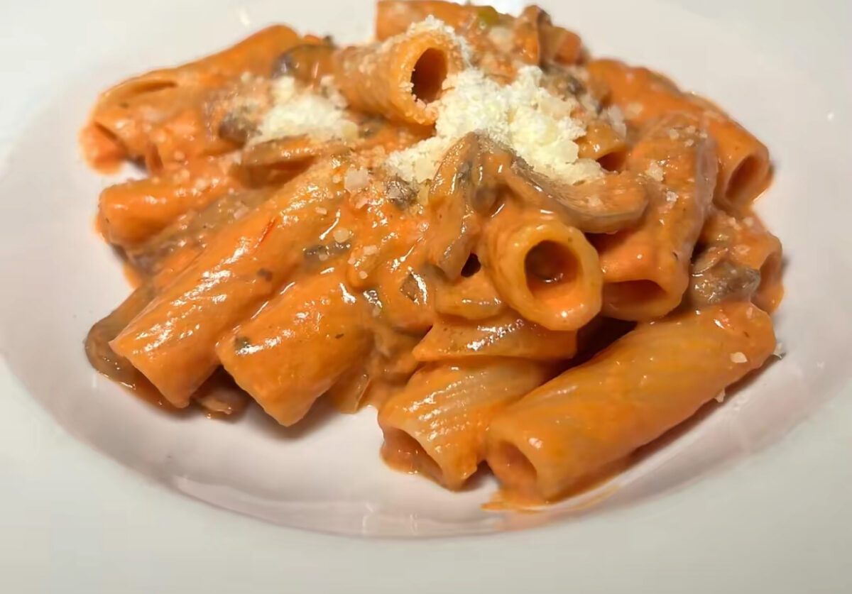 A bowl of Rigatoni alla Boscaiola from Antico Forno in Boston's North End, featuring ridged rigatoni in a creamy San Marzano tomato mascarpone sauce with mushrooms, sweet peas, and a dusting of Parmesan cheese.